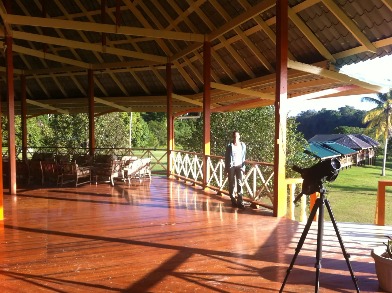 A wooden veranda with a spotting scope on a tripod looking out over a river lodge clearing
