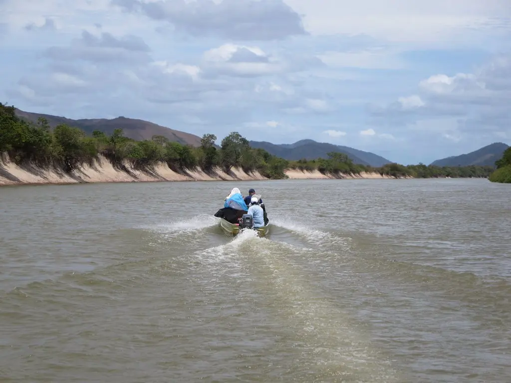 A small open boat travelling along the wide Rupununi River below low hills