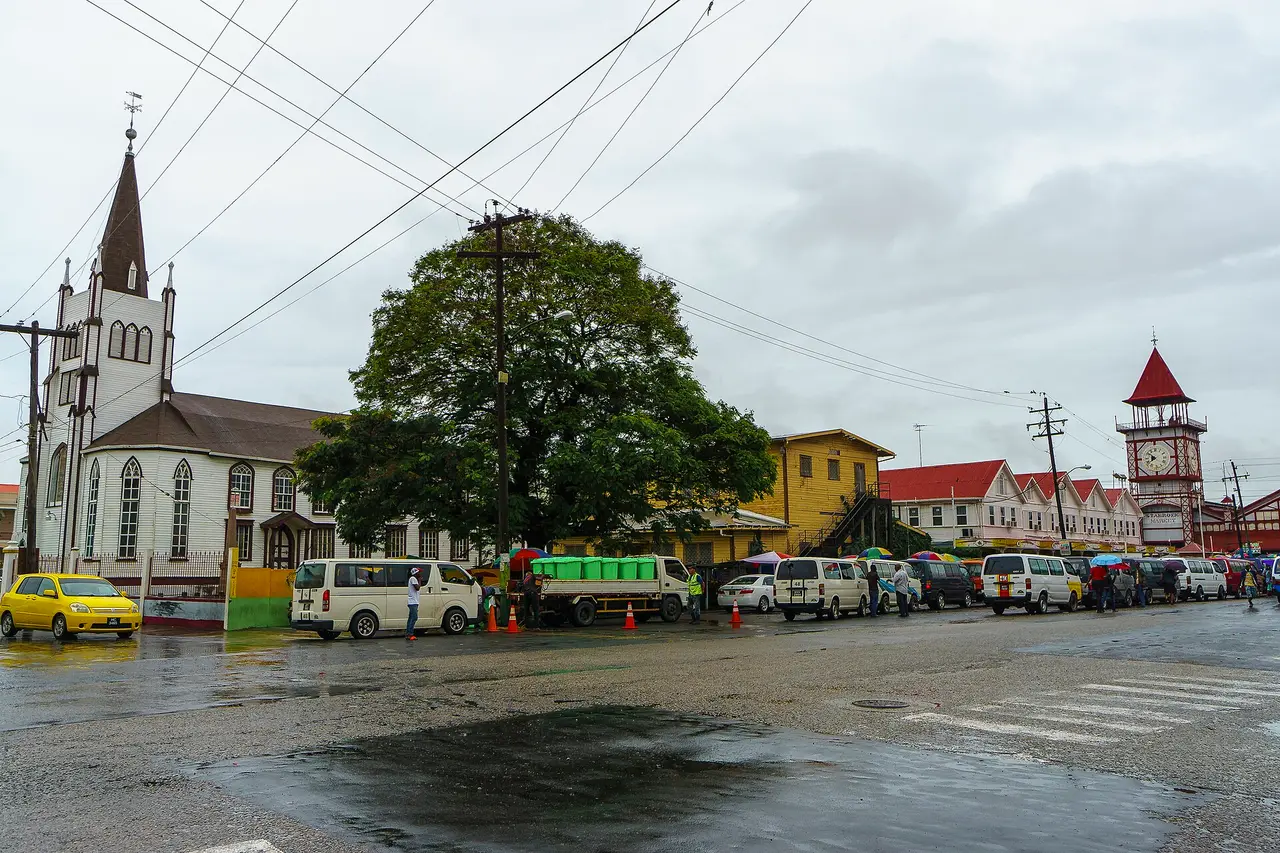 Street outside Stabroek Market in Georgetown with its clock tower, a white church and parked minibuses