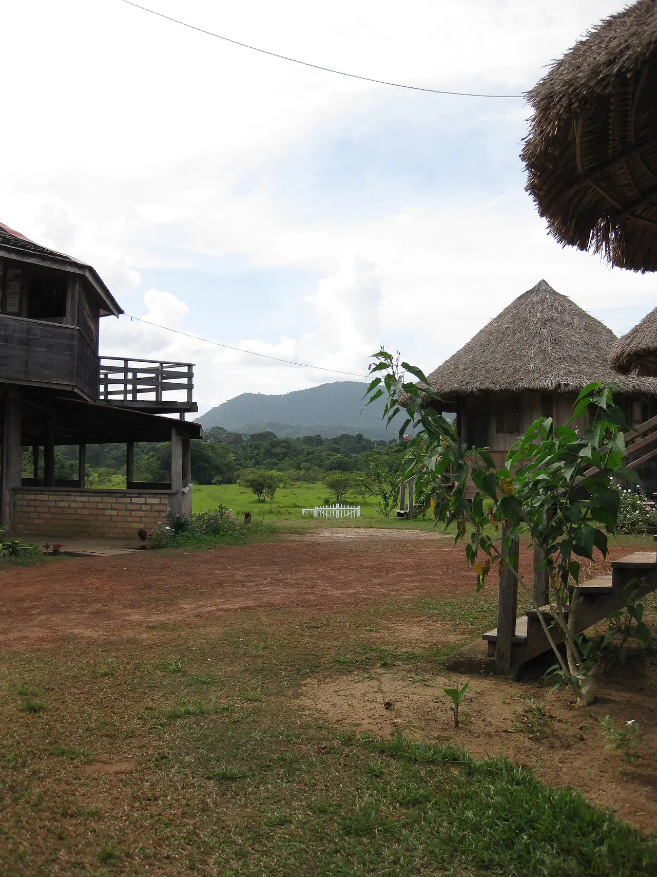 Thatched guest cabins and a timber building at Surama Eco-Lodge with savannah and hills behind